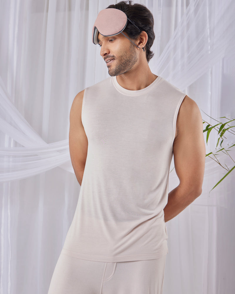 Man wearing a white sleeveless shirt and pants with a pink sleep mask against a white curtain background. Irish Cream mens AirKnit bamboo t-shirt ultra soft sustainable clothing